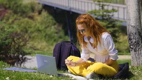 College student studying outdoors in the park completes her homework.
