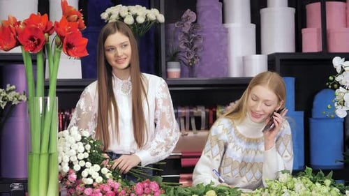 Two Female Florists Standing at a Table in Flower Workshop Holding a Bouquet of Flowers and Mixed