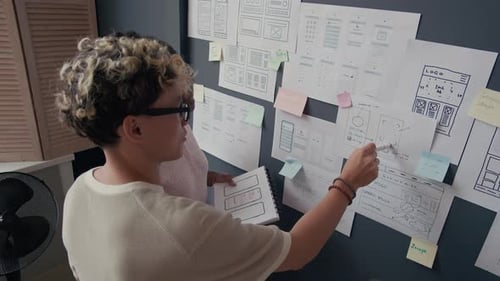 Asian Male UX Designer Discussing Mobile App Mockups with Colleague at Office