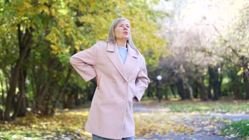 Woman experiencing back pain in autumnal city park