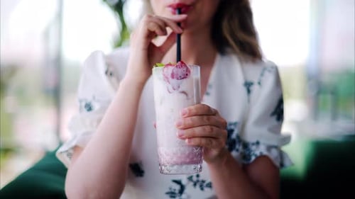 Woman drinking a strawberry drink with a black straw at a restaurant
