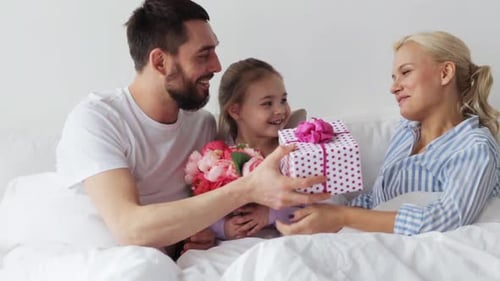 Happy family with gift and flowers in bed
