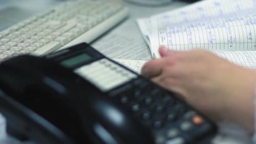 Woman Reviews Ledger at Desk with Phone, Keyboard