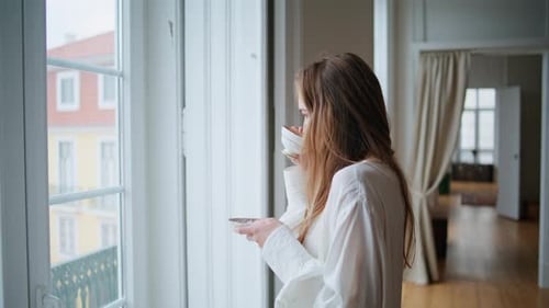 Woman in Apartment Drinking Tea and Looking out Window