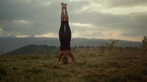 Sporty Girl Standing On Head In Mountain Landscape. Female Trainer Practicing Yoga On Ground. You...