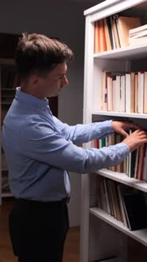 Vertical Video Man Reading a Book in a Library Surrounded By Knowledge