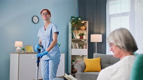 Woman Vacuuming as Senior Woman Reads in Living Room