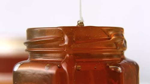 The Honey a Stream of Golden Honey Flows Into a Jar