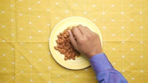 Person Picking Up Almonds From a Plate