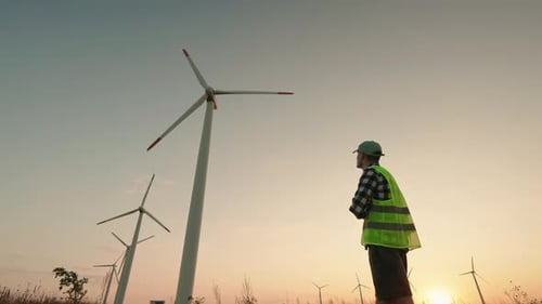 Technician in Reflective Vest and Helmet Observing Wind Turbines at Sunset