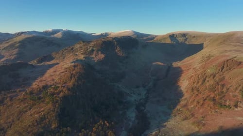 Mountains bathed in early morning sunshine with slow pan revealing range. High altitude view. Englis