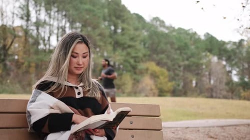 Asian Woman Reading a Book on a Bench at the Park in Autumn