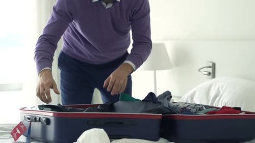Man packing suitcase on bed in hotel room