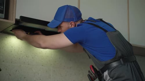 Réparateur réparant un extracteur de cuisine Un homme avec un tournevis à la main répare la hotte de cuisine