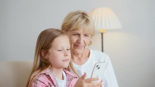 Child and Senior Woman Using Smartphone Together Indoors