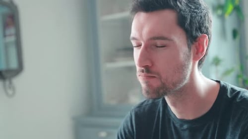 Young caucasian man bites into burger at home, cheeseburger eating enjoyment, close up portrait fast