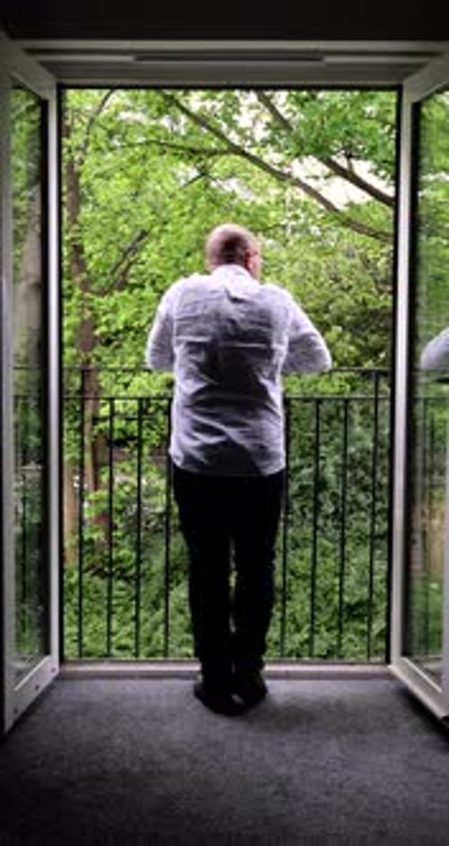 Portrait footage of middle aged man standing by a hotel apartment balcony looking out to a wooded