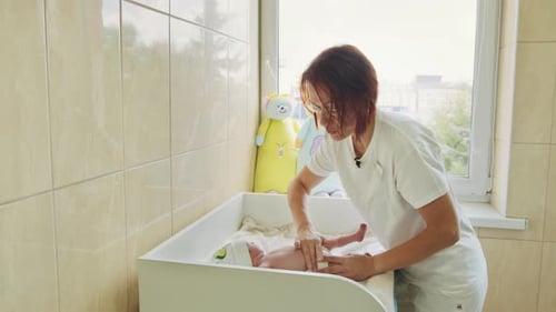 Female Doctor Massaging Tummy of Newborn Baby in Clinic