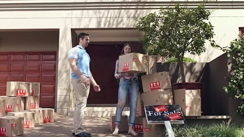 Couple Moving Boxes Into Sold Suburban Home
