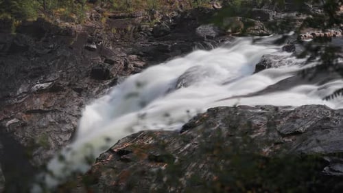 A powerful and tumultuous waterfall cascades in the rocky riverbed amidst the summer forest. Long ex