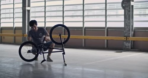 Male BMX Rider Checking Wheel of Bike in Parking Lot
