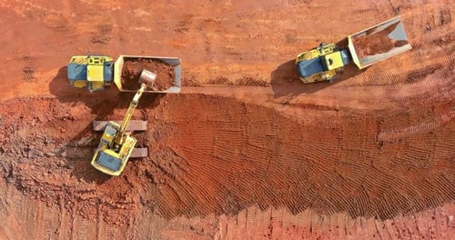Excavadoras para operaciones pesadas de movimiento de tierras que cargan volquetes en un sitio de tierra roja