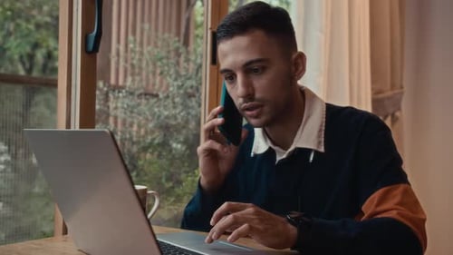 Young Adult Working From Home Using Laptop And Cellphone