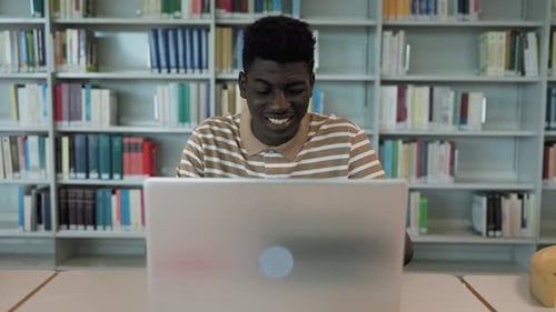 Young African student using laptop in library - School education concept