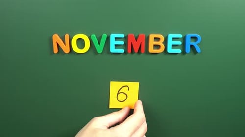 Hand sticking a sticker 6 November calendar day on school board. 6 date of November. Sixth day
