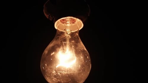 Incandescent Bulb on Wire Turns On and Off and Flickers on Black Background