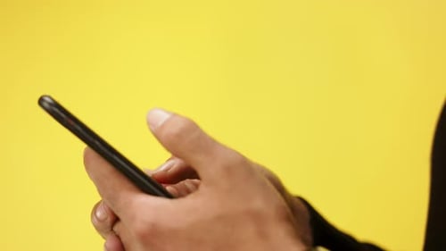 Closeup Shot Of Unrecognizable Man Using Smartphone In A Studio On Yellow Background.