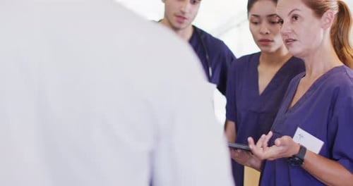 Video of diverse group of male and female doctors looking at tablet talking in hospital corridor