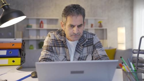 Mature focused man working in home office using laptop, typing on keyboard.
