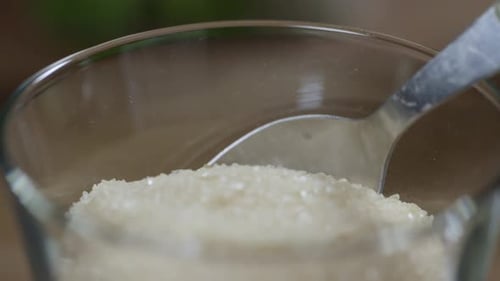 Close-up of brown sugar in a glass. A spoon stirs the sugar. No face.