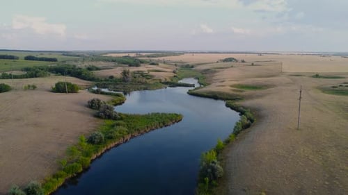 Ein ruhiger Fluss, der sich durch üppige Felder in einer malerischen Landschaft schlängelt, die von einer Drohne aufgenommen wurde