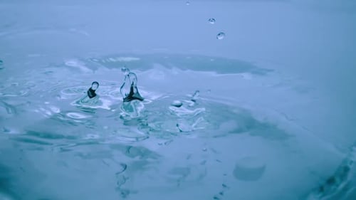 Macro Shot of a Drops of Water Falls on a Blue Liquid Surface Creating Water Rings and Waves