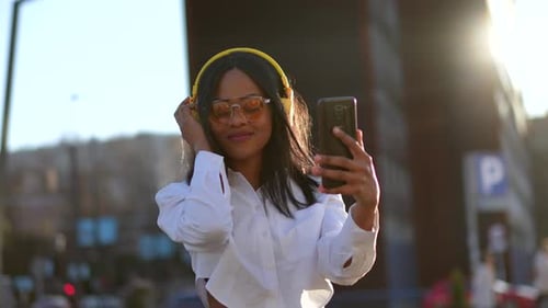 African american woman listening to music with headphones at sunset in the city