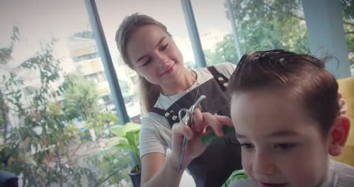 Fashionable Hairdresser Cuts a Child's Hair with a Clipper in a Barbershop Close Up Side View
