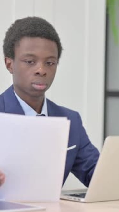 Young Man Works with Laptop and Paperwork at Desk