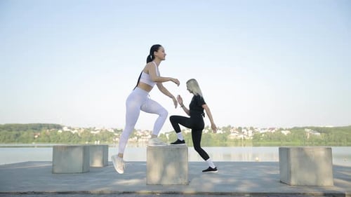 Fitness Together Two Women Do Fitness on the Shore of the Lake on Large Stones in a Warm Sunny Day