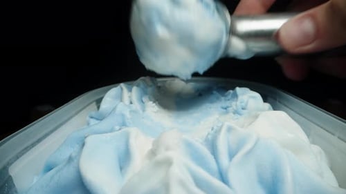 Using a special metal spoon, I create a scoop of blue and white ice cream, close-up shot.