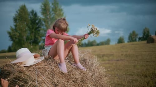 Girl with Flowers Sitting on Hay Bale