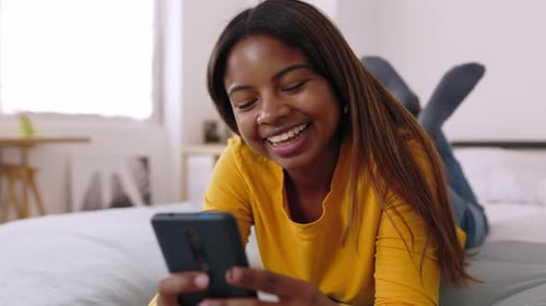 Woman Smiling Using Phone While Lying on Bed
