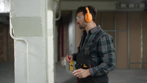 Man Builder Engineer Repairman Using Measuring Tape on Construction Site Building Check Wall