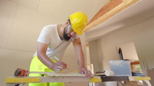 A Hardworking Construction Worker is Measuring Wood While Wearing a Bright Yellow Safety Helmet