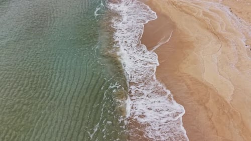 Waves crash on sandy shore at sunny beach during daytime hours