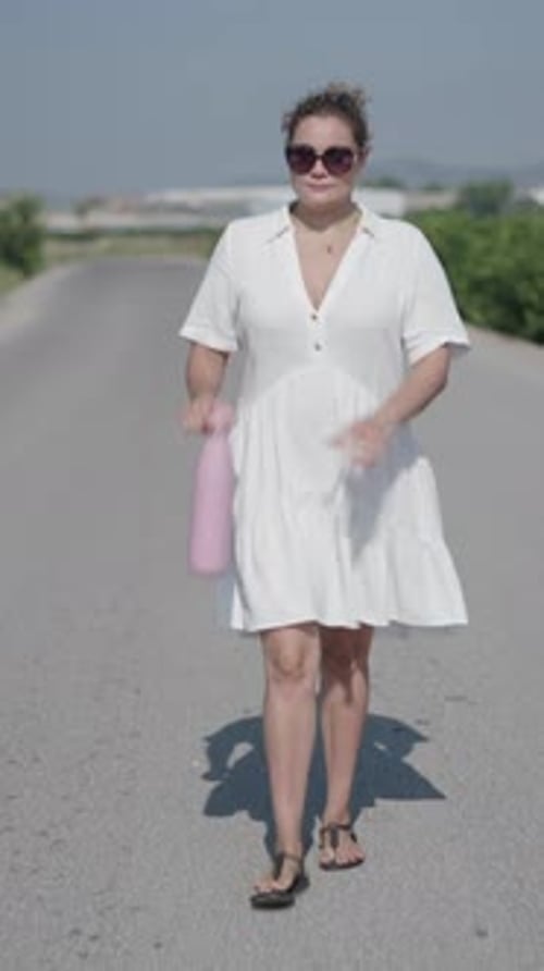 Woman Walking on Rural Road Drinks Water