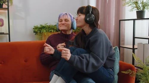 Lesbian Women Family Couple in Wireless Headphones Dancing Disco Listening Music Song on Home Couch