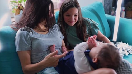 Mutter und Tochter sitzen auf der Couch und interagieren sanft mit einem Baby auf dem Schoß der Mutter,