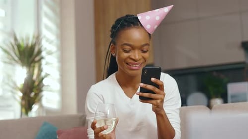 Woman wearing birthday hat video calling with champagne